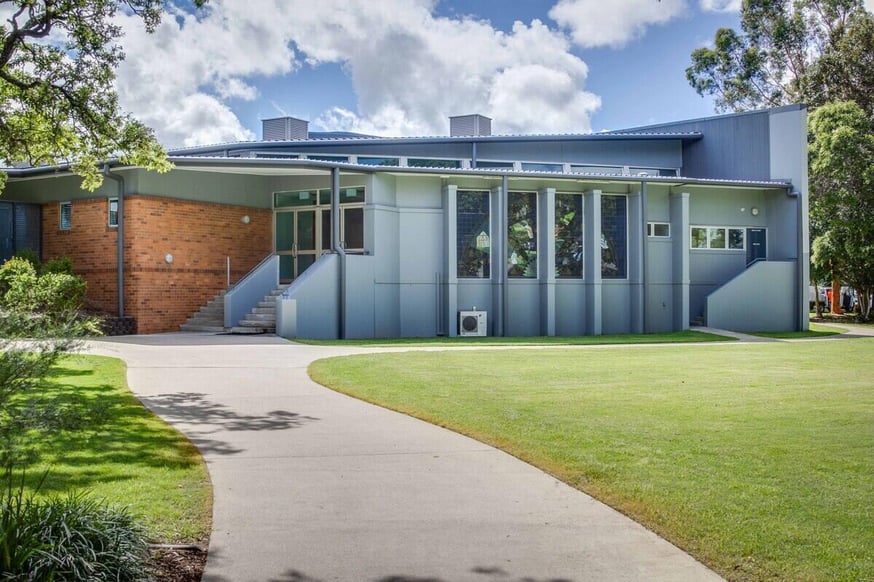 A modern building with blue and brick walls, fronted by a green lawn and a curved concrete path.