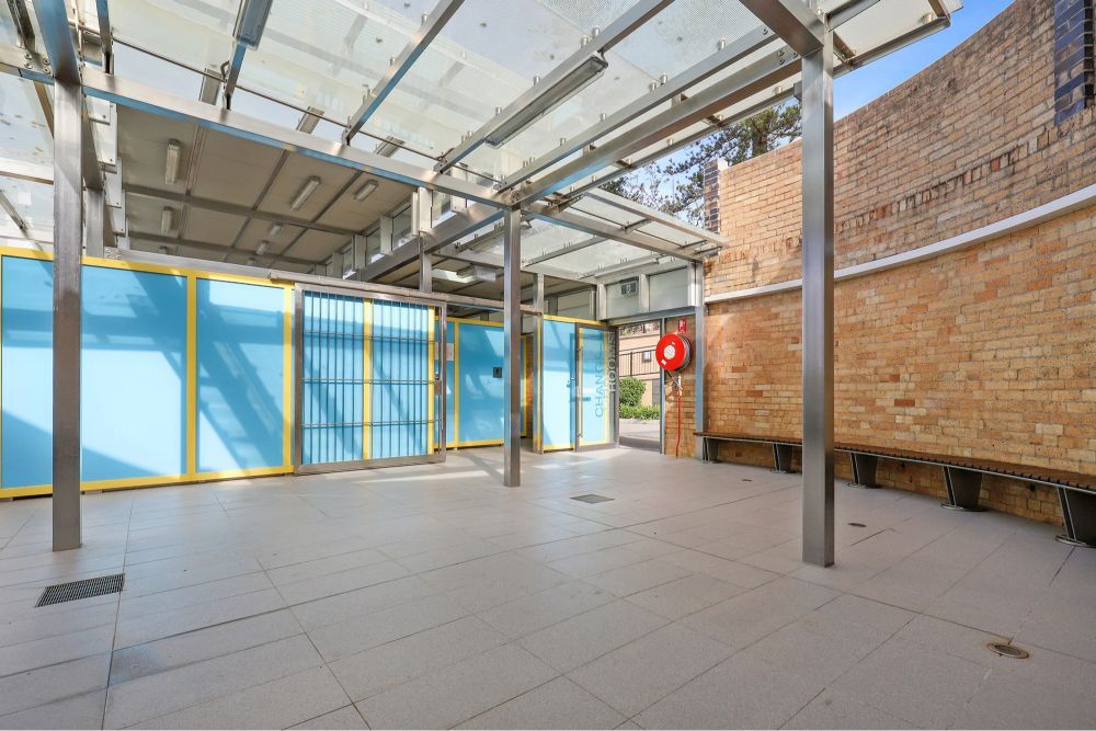 Covered pavilion area with blue change room doors, benches, and a brick wall.