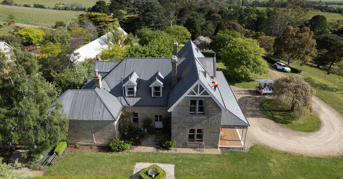 Aerial shot of a large stone country house with workers on the roof.