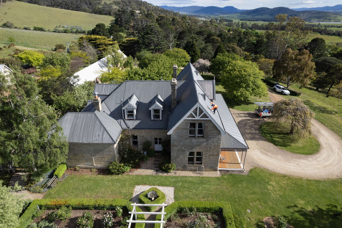 Aerial shot of a large stone country house with workers on the roof.