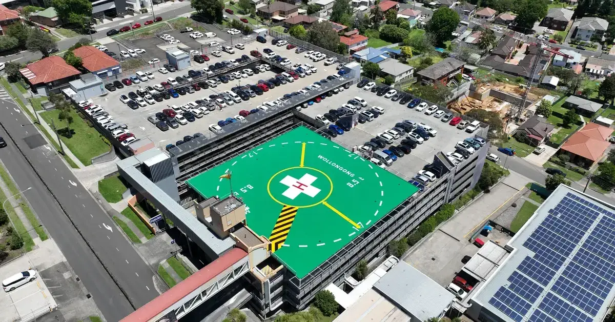 Aerial view of a hospital car park with a bright green helipad on the roof.