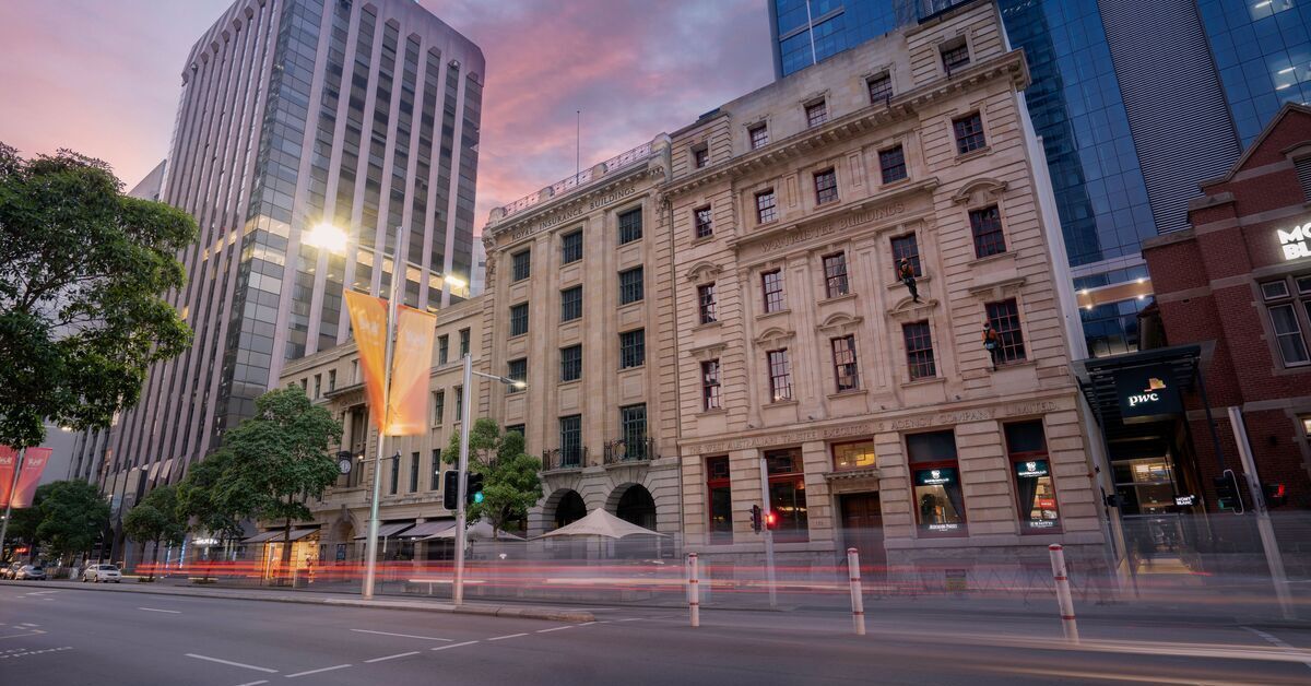 A long-exposure shot of a city street at dusk, showing heritage buildings next to modern skyscrapers.