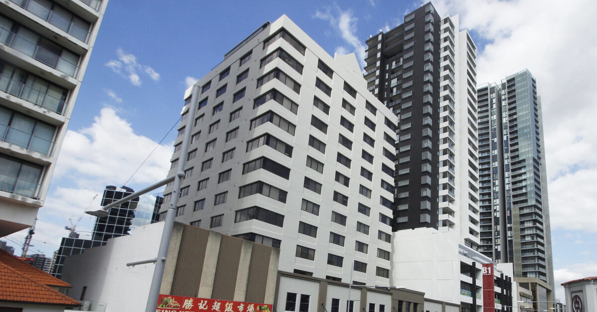 Street view of tall city buildings above a row of shops, including an Asian grocery.