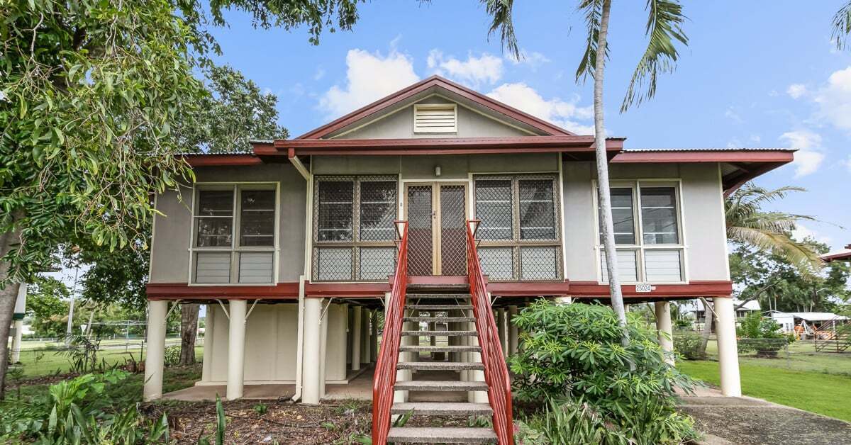 A high-set house on stilts with a central red staircase leading to the front door.
