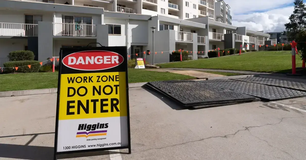 A Higgins 'DANGER WORK ZONE DO NOT ENTER' sign on a pavement in front of an apartment complex.
