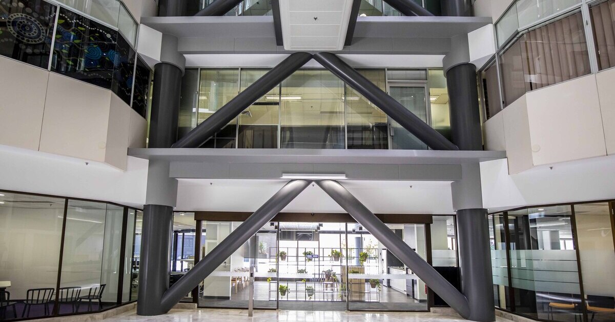 The interior atrium of a modern office building featuring large, grey structural support beams.