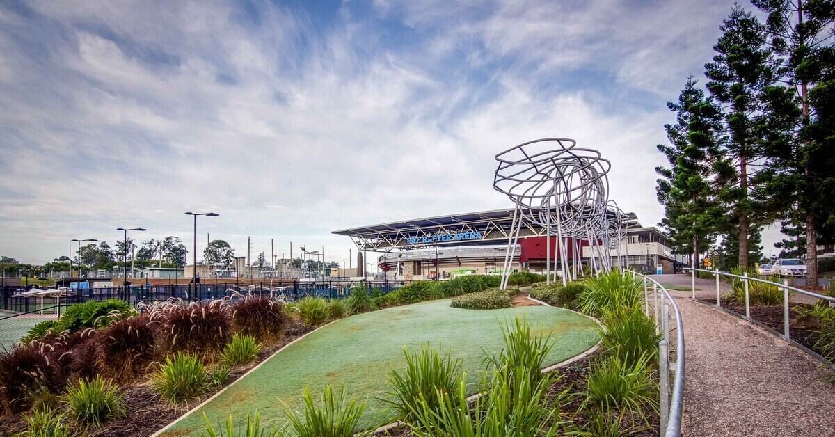 A landscaped path with a large metal sculpture leads towards the Pat Rafter Arena.