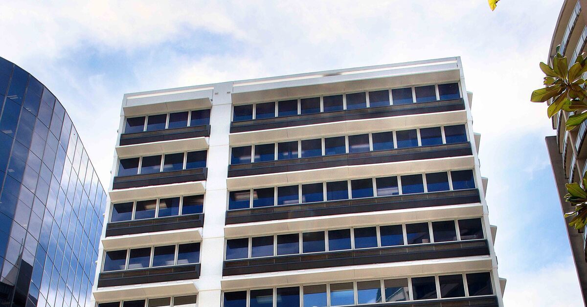 A street-level, low-angle view of a tall, white multi-storey office building.