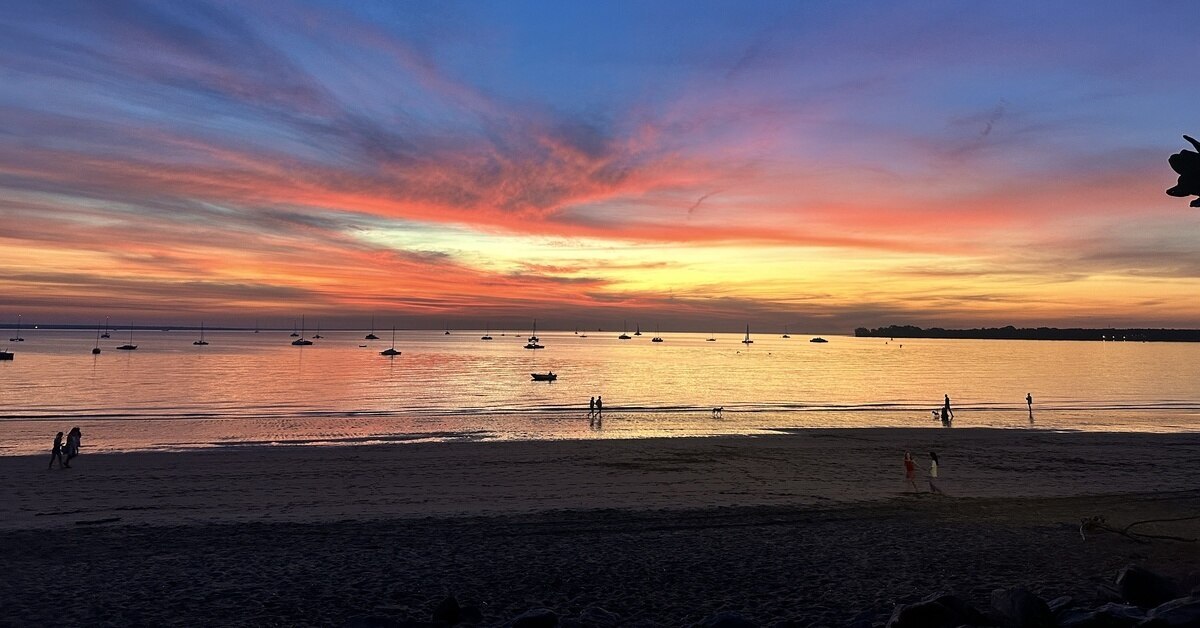 A vibrant orange and blue sunset reflecting on a calm bay with sailboats.