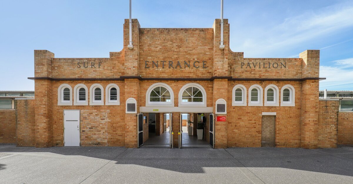 The symmetrical front entrance of a large, brick surf pavilion building.
